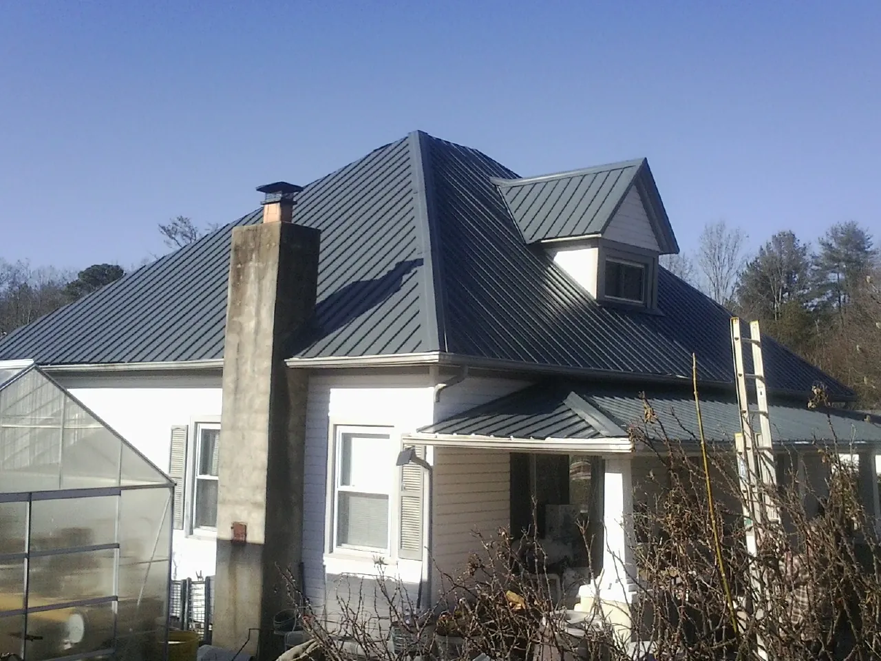 Dark blue standing seam metal roof on a white farmhouse with dormer — Slate & Tile Roof Repair by Roofing Brothers in Duarte