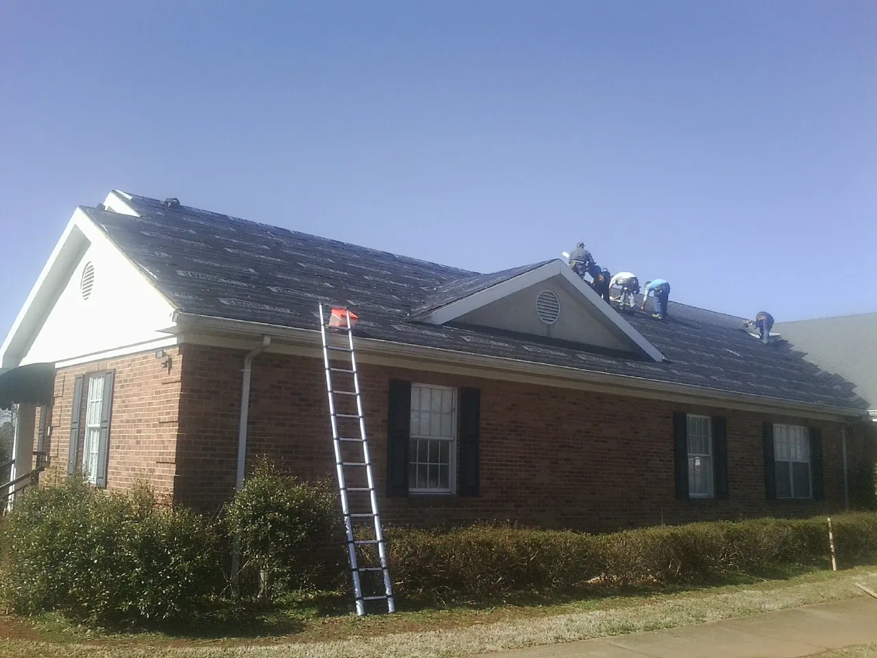 Crew tearing shingles off a brick ranch roof with a ladder set — Emergency Roof Repair work by our crew in Duarte
