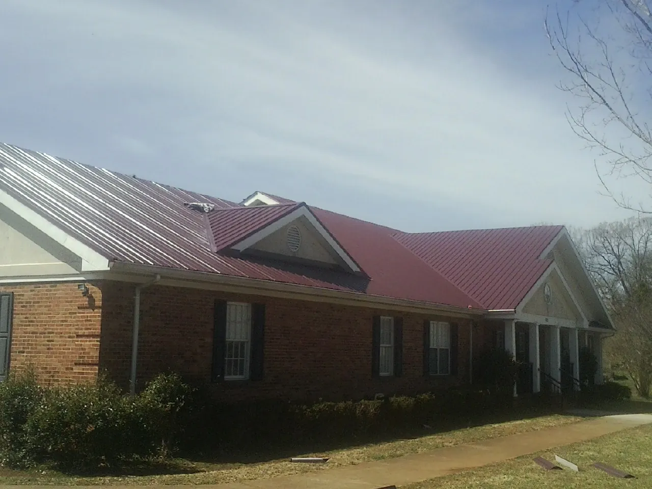 Red metal roof with gabled entries on a long brick building, from a Hail Damage Roof Repair job in Duarte