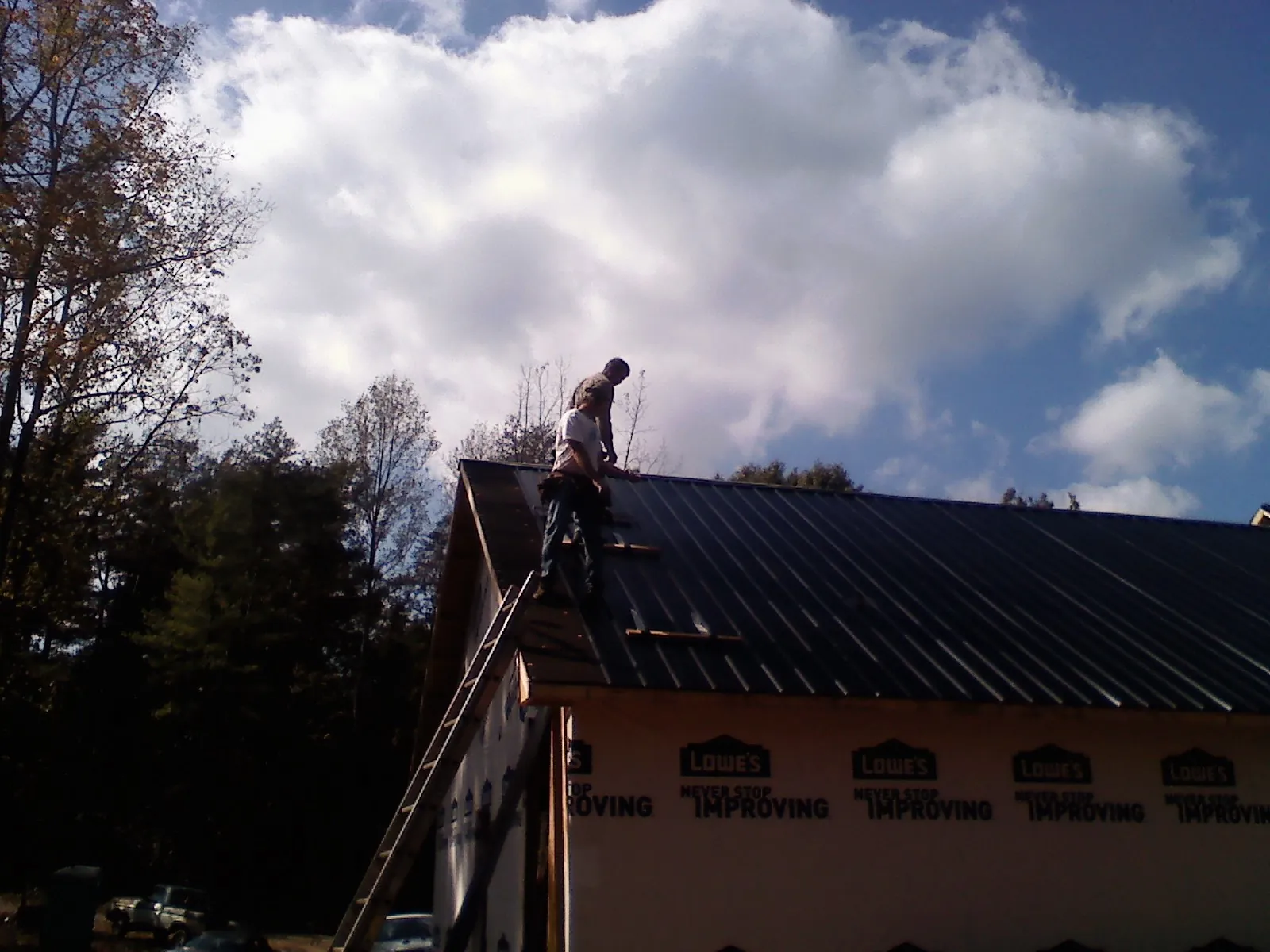 Roofer fastening dark metal panels high against a cloudy sky, from a Roof Inspection job in Duarte