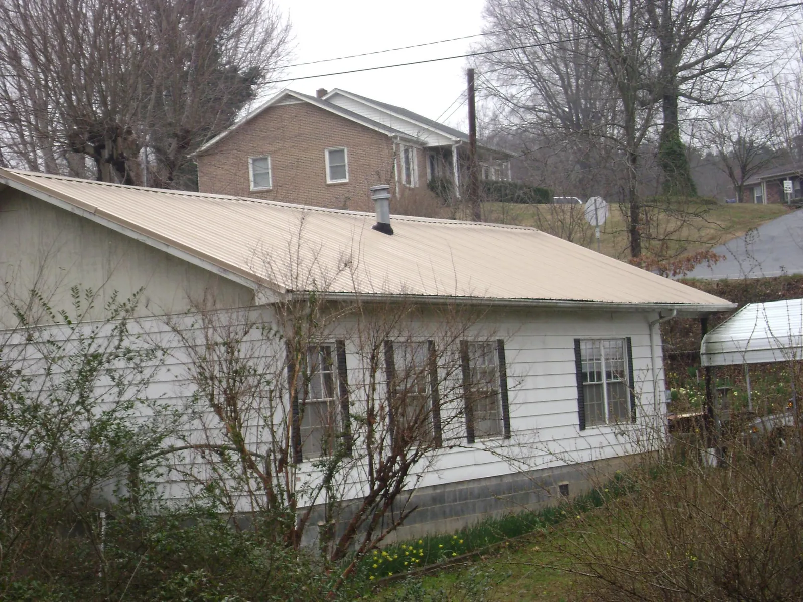 Tan metal roof on a white sided house set into a hillside — Commercial Roofing by Roofing Brothers in Duarte